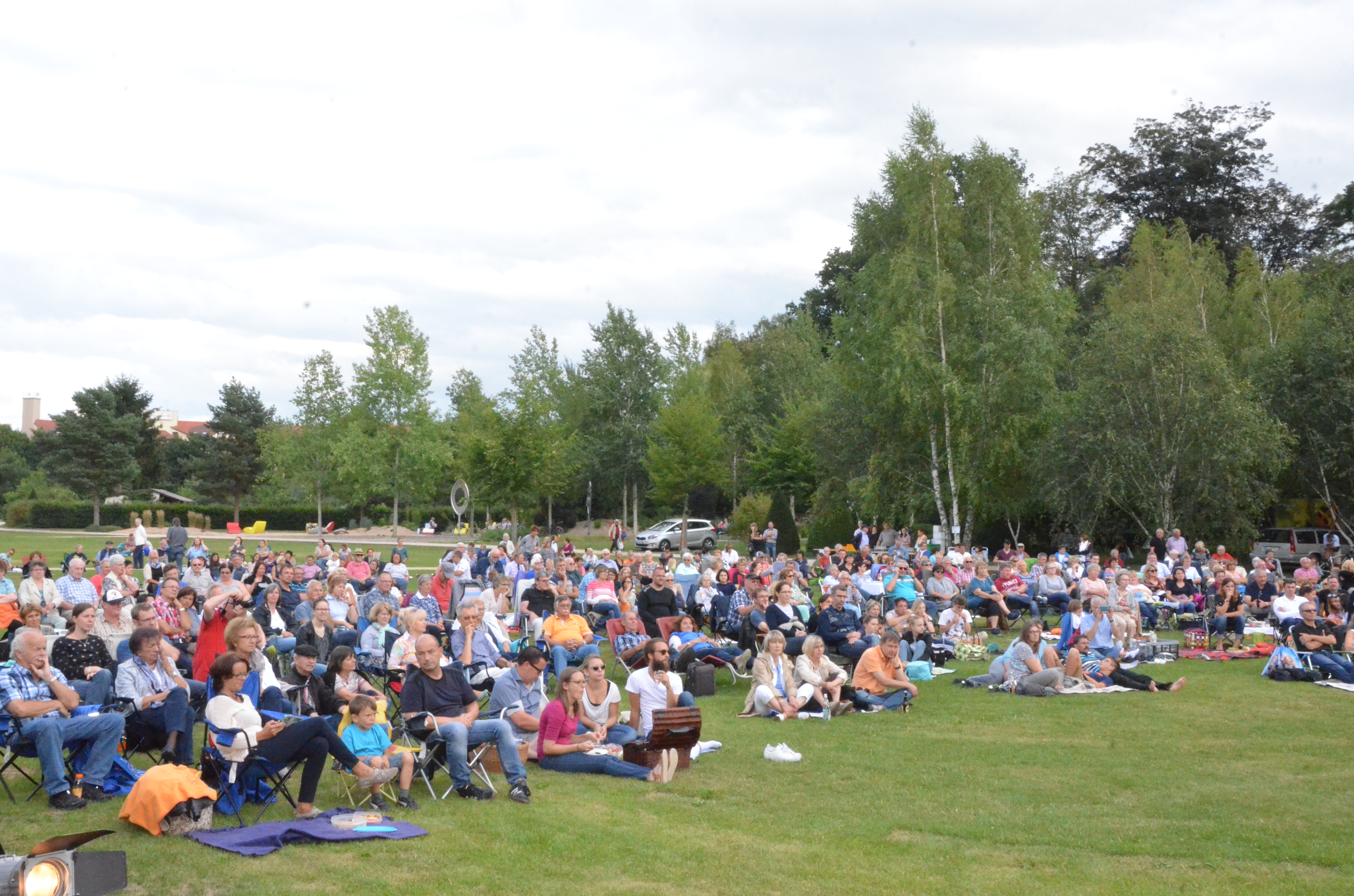  Zuschauer der Sommerserenade sitzen mit Picknickdecken auf der Wiese und lauschen dem Konzert 